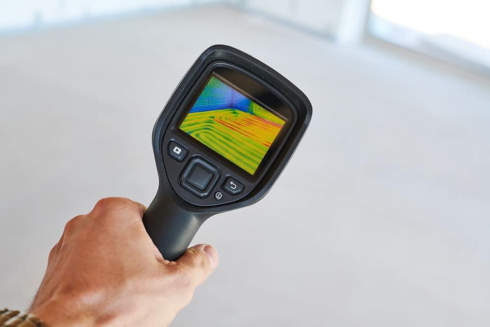 Handheld thermal camera scanning a floor for hidden moisture